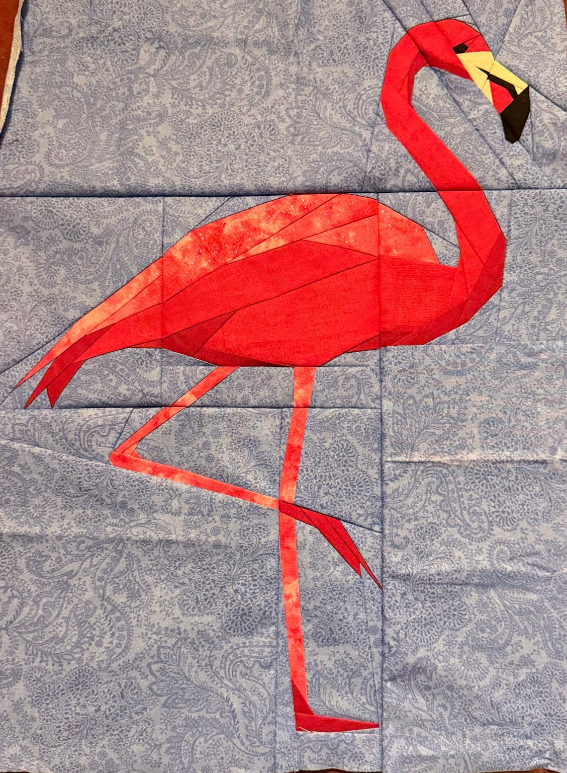 Sewn Flamingo foundation paper piecing quilt top in red and coral fabrics on a blue paisley background, by Quilts of Whimsy.